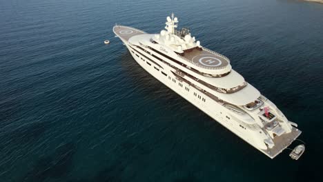Aerial-orbit-over-the-Dilbar,-third-largest-private-luxury-ship-owned-by-the-Russian-billionaire-oligarch-Alisher-Usmanov-anchoring-on-the-emerald-waters-near-Porto-Cervo-in-Sardinia