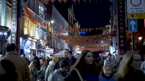 Rows-of-beautiful-traditional-Chinese-lanterns-hung-across-the-street-in-China-Town-London,-below-crowds-of-people-out-and-about-enjoying-a-pleasant-winters-evening,-England