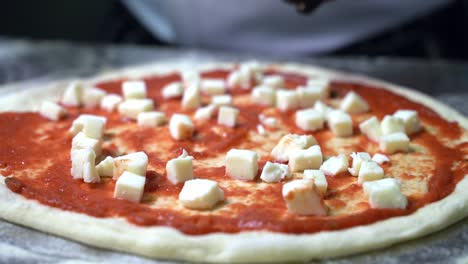 Preparing-and-adding-mozzarella-cheese-on-a-pizza-dough-with-tomato-sauce