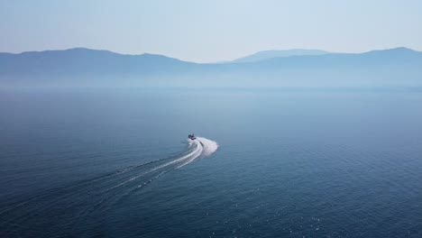 Speed-boat-driving-fast-in-curves-over-deep,-blue-Okanagan-Lake-on-a-hot-day-during-Canadian-wildfire-season