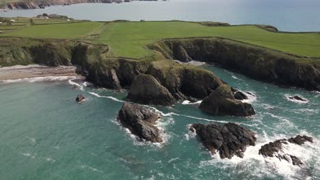 Drone-shot-of-waves-hitting-into-rocks-on-a-small-headland-in-Ireland-on-a-summer's-day