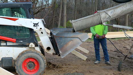 Construction-worker-pours-wet-cement-into-bucket-of-skid-steer-loader