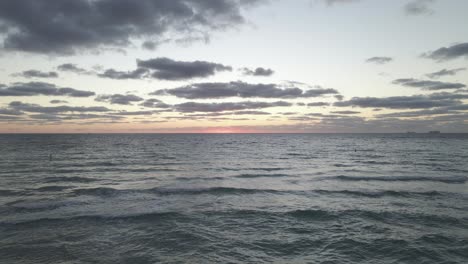 Pink-orange-horizon-over-calm-dark-water,-dawn-over-sandy-ocean-beach