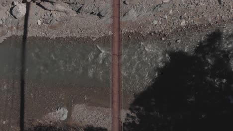 Zwei-Personen-Gehen-über-Eine-Metalldrahtseil-Hängebrücke-über-Felsiges-Flusswasser,-Das-Das-Bergtal-Kabayan-Benguet,-Philippinen,-Von-Oben-Nach-Unten-Aus-Der-Vogelperspektive-Im-Weitwinkel-Fließt