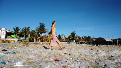 Kaukasische-Frau,-Die-In-Sandalen-Am-Verschmutzten-Strand-Mit-Plastiktütenabfällen,-Giftigem-Müll,-Meeresverschmutzungskonzept-Und-Globaler-Erwärmung-Spaziert