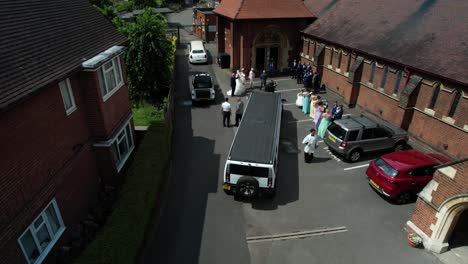 Wedding-ceremony-guest-aerial-reversing-view-at-quaint-church-townscape-as-priest-walks-towards-camera