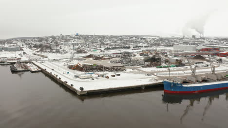 Aerial-rise-over-a-recycling-center-and-freighters-docked-in-port-during-winter
