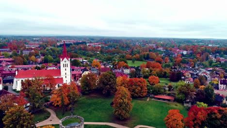 Aerial-backward-moving-view-of-a-medieval-castle--Cēsis-Castle-in-Latvia-surrouned-by-autumnal-trees-on-a-cloudy-day