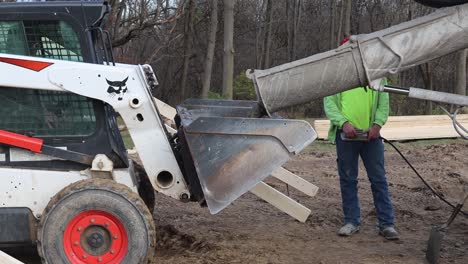 Construction-crew-pouring-wet-cement-into-bucket-of-skid-steer-loader