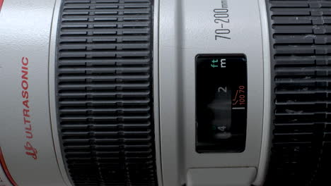 Close-Up-Shot-Of-Lens-Focus-Window-On-Canon-L-Telephoto-Lens,-tracking-along-the-body-revealing-the-focus-ring