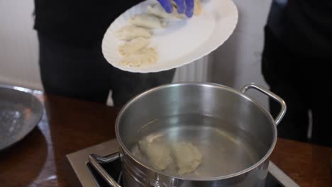 Dropping-fresh-handmade-pasta-dumplings-in-hot-boiling-pot-water,-chef-hands-wearing-gloves-in-professional-kitchen-close-up