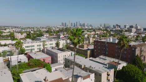 Flying-Through-Palm-Tree-Lined-Neighborhood-Towards-Downtown-Los-Angeles-Skyline