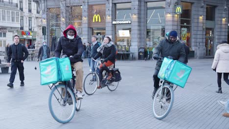 Two-African-American-Deliveroo-riders-deliver-food-orders-for-customers-in-city-center-of-Brussels,-Belgium---Slow-motion