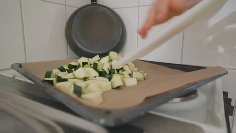 Man-putting-chunks-of-zucchini-on-a-baking-sheet