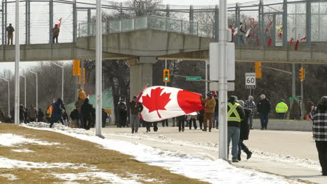 12-February-2022---Freedom-Convoy-Protestors-Walking-Across-Road-Carrying-Large-Canadian-Flag