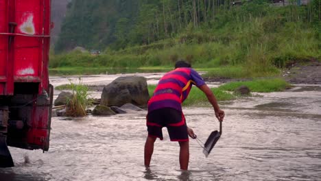 Close-up-shot-of-male-worker-picking-sand-out-of-river-and-put-on-truck-at-Bego-Pendem-in-Indonesia