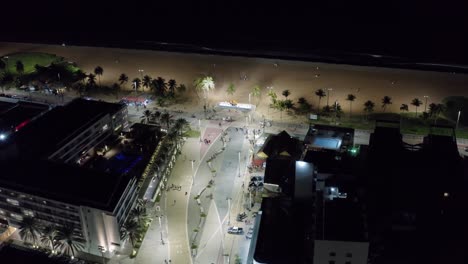 Rotating-aerial-night-shot-of-the-main-plaza-in-the-center-of-Tambaú-with-the-city-sign,-a-boardwalk-along-the-beach,-restaurants,-and-apartments-in-the-capital-city-of-Joao-Pessoa,-Paraiba,-Brazil