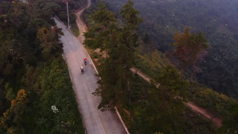 2-motorcycles-leave-road-to-dirt-trail-in-guatemala-mountains-aerial-chase-cam