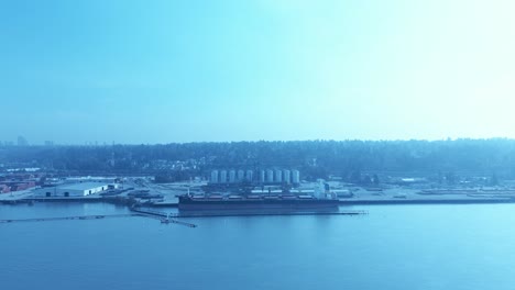 aerial-4k-drone-flyover-river-port-pacific-channel-freighter-from-the-Ukraine-docked-and-loading-raw-ingredients-for-bread-supplies-from-silos-with-portable-wet-docks-surrounded-ship-to-secure-export