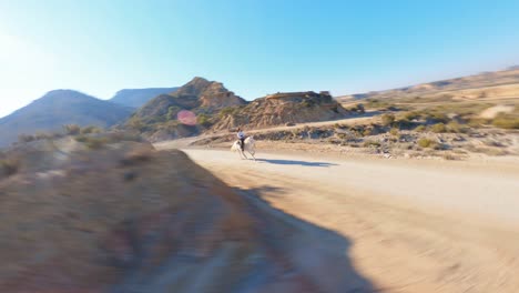 FPV-drone-flying-fast-around-a-woman-riding-a-horse-through-a-rugged,-desert-landscape