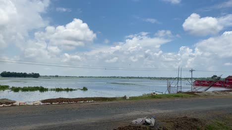 Footage-while-driving-by-a-flooded-area-in-Sylhet,-Bangladesh-with-a-stunning-blue-clouded-sky-overhead