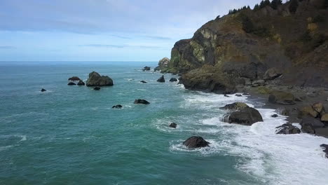 Stationary-aerial-drone-of-Pacific-Northwest-rocky-coastline,-cliffs,-and-beach-on-overcast-day