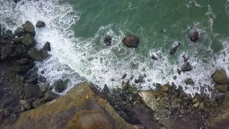 Aerial-Birdseye-view-of-Pacific-Northwest-rocky-coastline,-waves-crashing-and-green-seas