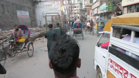 Blick-Aus-Der-Ersten-Person-Von-Einem-Rikscha-Beifahrersitz-Aus,-Während-Ein-Rikscha-Fahrer-Oder-Fahrer-Durch-Die-Belebten-Straßen-Von-Dhaka,-Bangladesch,-Fährt