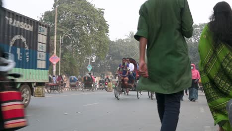 A-low-angle-view-of-numerous-cars,-motorcycles,-rickshaws,-and-pedestrians-driving-and-walking-through-a-busy-road-in-Dhaka,-Bangladesh