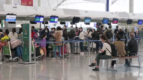 Chinese-flight-passengers-sit-on-a-bench-as-other-travelers-check-in-at-the-airline-desk-counter-in-the-background-at-the-Hong-Kong-international-airport