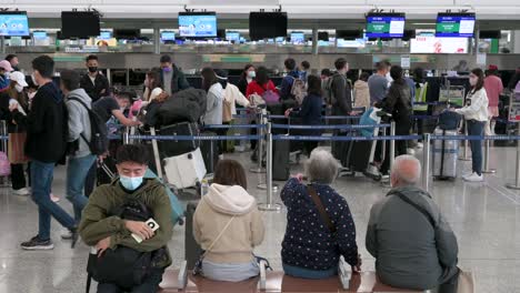 Flight-passengers-sit-on-a-bench-as-other-travelers-check-in-at-the-airline-desk-counter-in-the-background-at-the-Hong-Kong-international-airport