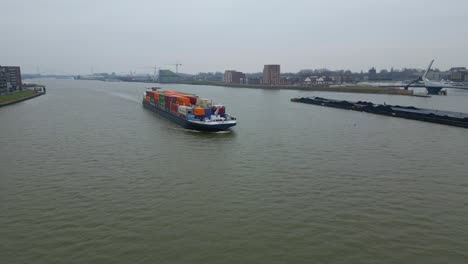 Luftdrohnenaufnahme-Des-Sich-Nähernden-Containerschiffs-Scaldis,-Das-An-Einem-Bewölkten-Tag-In-Dordrecht-Entlang-Der-Oude-Maas-Fährt