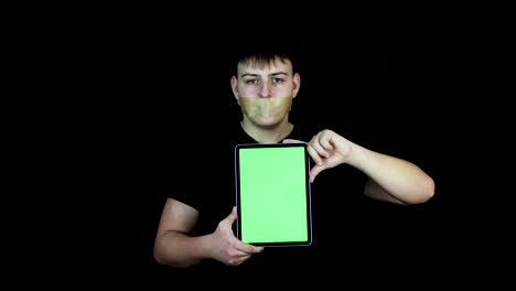 Teenager-Mit-Klebeband-über-Dem-Mund,-Der-Ein-Tablet-Mit-Grünem-Bildschirm-Hält