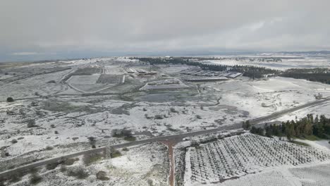 Panoramic-aerial-drone-view-of-snow-covered-countryside-and-farmland,-Ortal,-Israel