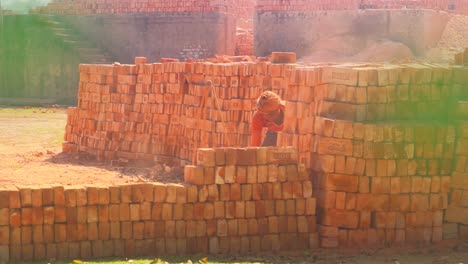 A-brick-worker-stacks-new-bricks-on-a-big-pile,-creating-dust-clouds-in-the-air,-exemplifying-the-hard-work-of-labor