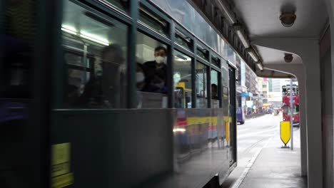 Double-decker-tramway-cars-pass-by-stop-in-central-Hong-Kong,-static
