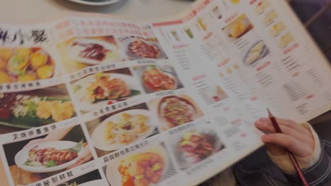 Restaurant-customer-looking-through-Chinese-restaurant-menu-with-numerous-options