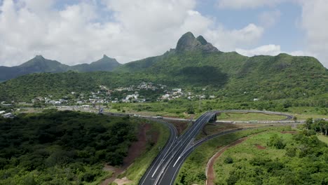 Aerial-forward-flight-over-green-landscape-of-Mauritius-with-highway-bridges-and-mountains-in-background