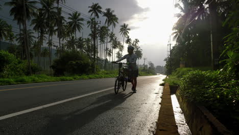 Bikepacker-woman-walks-bike-along-tropical-southeast-asia-road
