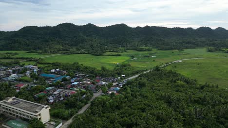 A-stunning-aerial-view-captures-the-edge-of-a-village-and-surrounding-rural-landscape,-with-forested-mountains-in-the-distance,-showcasing-the-beauty-of-nature-and-countryside