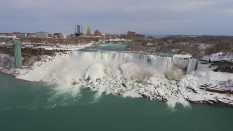 Wide-aerial-parallax-of-Niagara-Falls,-bridge-and-icy-cliffs-in-winter