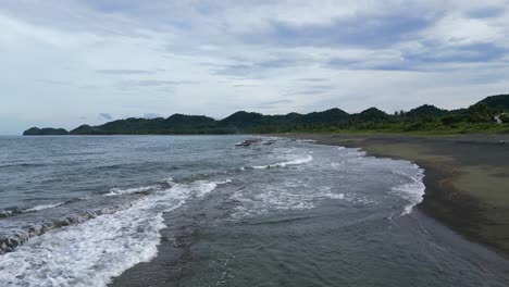 Aerial-footage-flies-low-over-the-crashing-waves-and-onto-the-beach-of-Catanduanes,-capturing-the-raw-power-and-beauty-of-the-ocean