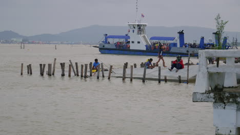 Ferry-boat-turning-around-with-people-relaxing-on-pier-in-front,-Songkhla-ferry,-Thailand