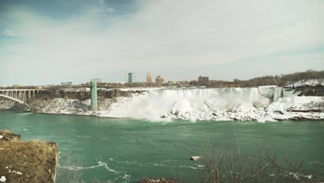 Icy-Niagara-Falls-from-across-the-water-in-winter,-wide-handheld-shot