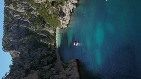 The-Calanque-d'En-Vau-beach-secluded-between-rugged-cliffs-near-Cassis,-France---aerial-flyover-in-vertical-orientation