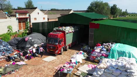Aerial-shot-of-a-truck-loaded-with-bags,-unloading-old-clothes-and-a-person-guiding-on-the-ground