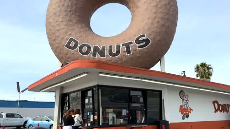 Famous-Randy's-Donuts-in-Inglewood,-Los-Angeles-USA,-Giant-Doughnut-and-Store-Front-With-People