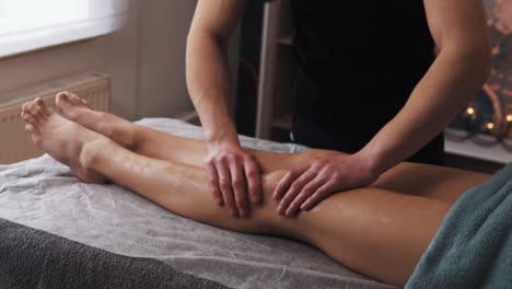 Hände-Eines-Männlichen-Masseurs,-Der-In-Einem-Massageraum-Mit-Sanftem-Licht-Eine-Sanfte-Massage-Der-Beine-Einer-Frau-Durchführt