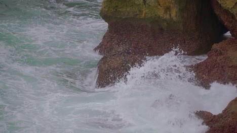 Ocean-whitecap-waves-crashing-on-rocks-at-base-of-cliffs,-closeup-view,-Indonesia