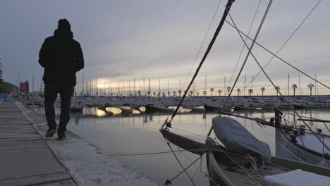 Man-takes-photo-of-docked-boats-in-harbor-during-dusky-weather,-static-shot-port